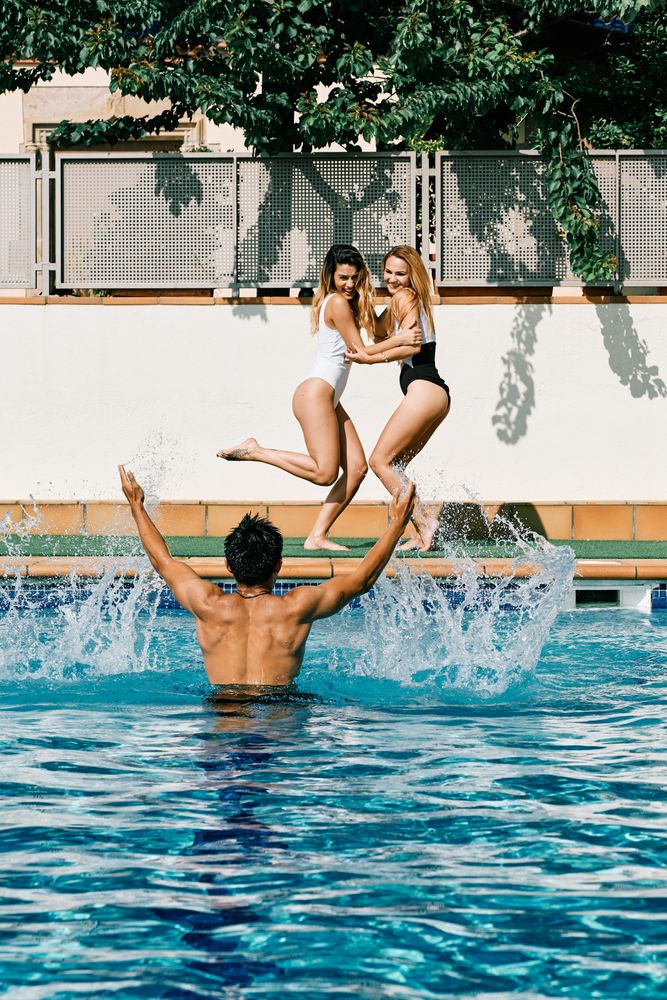 a young man by the pool throwing water to two young models