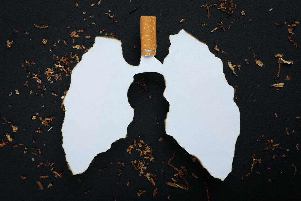 Ripped paper in lung shape with cigarette and tobacco on dark background