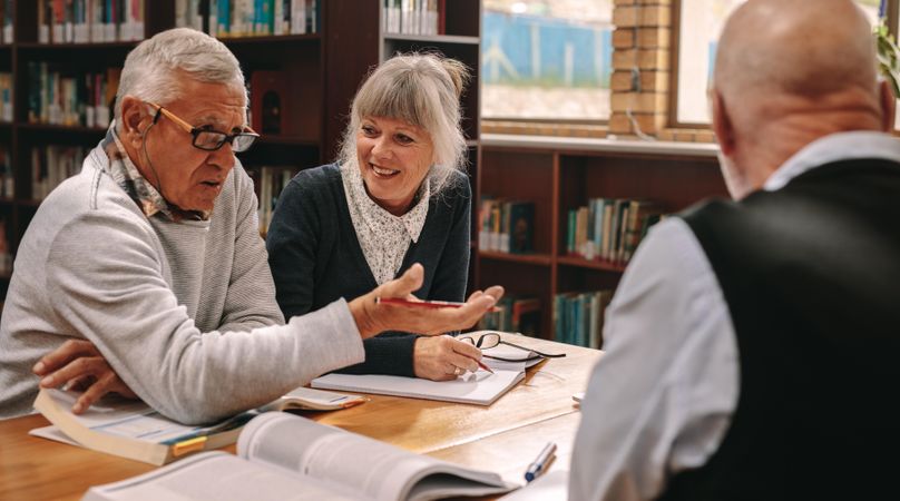 Group of mature people sharing ideas and discussing subject sitting in a library