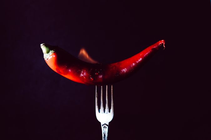 red chili pepper on fire in fork on a dark background