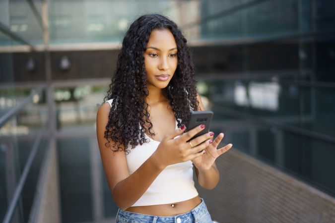 A Young Woman Engaged with Her Smartphone in a Vibrant Modern Urban Setting During the Day