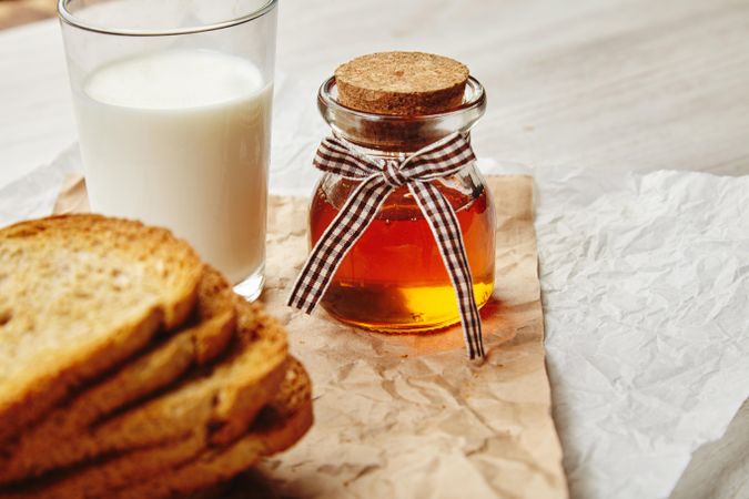 Pot of honey with stack of toast and glass of milk