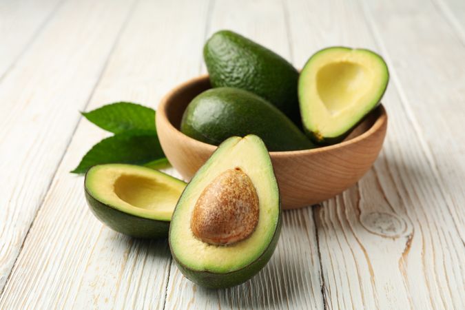 Bowl with fresh avocado on wooden background, close up