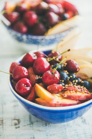Close up top view of blue bowl of fresh fruit with cherries, peaches, blueberry