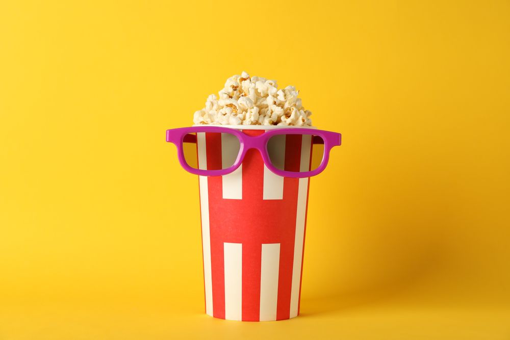 Striped bucket with popcorn and 3d glasses on yellow background, copy space