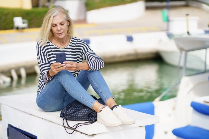 Mature woman using her smartphone sitting on the pier