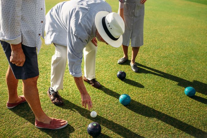 Man in hat bending down to pick a boules in a lawn