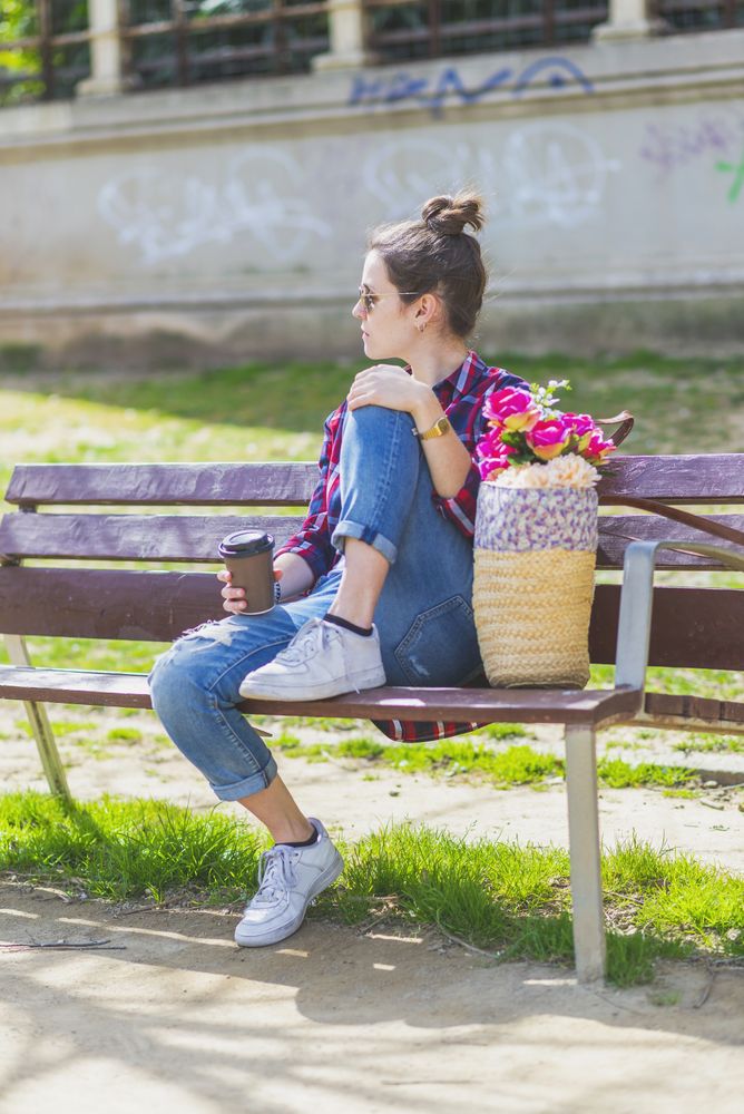 Side view of a young hipster woman sitting on a park bench relaxing in a sunny day while looking away