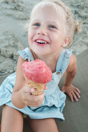 Cheerful girl eating ice cream while resting on beach