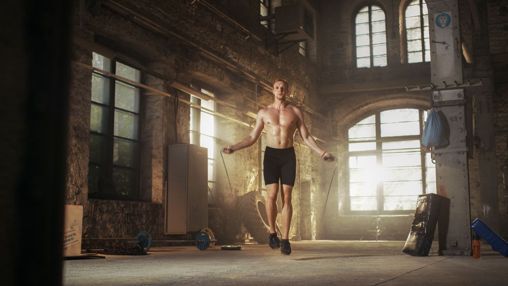 Athletic Shirtless Fit Man Exercises with Jump   Skipping Rope in a Deserted Factory Hardcore Gym.