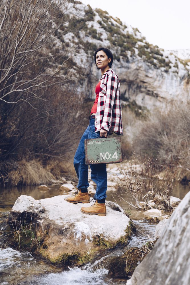 Woman with case jumping on rocks above stream