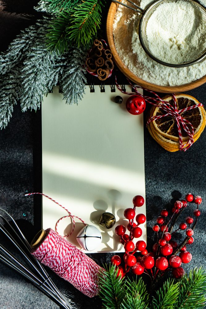 Notebook on kitchen table surrounded by baking ingredients and Christmas decorations