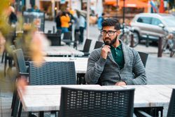 Man in gray sweater wearing eyeglasses sitting on dining table outdoor