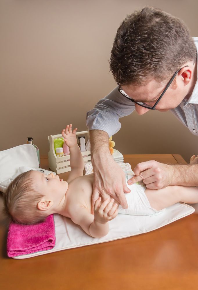 Father fastening diaper of baby, vertical