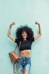 Female wearing casual clothes leaning on turquoise wall and smiling with her arms in the air