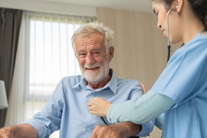 Smiling older male having chest examined by Asian medical professional