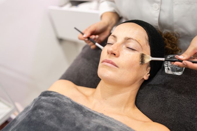 Crop of beautician applying cleansing oil on client in beauty center
