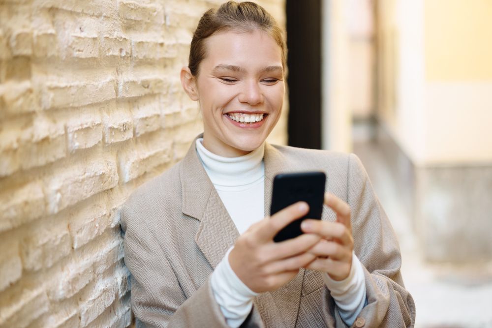 A Joyful Young Woman is Engaged with Her Smartphone While in a Modern Urban Setting Today