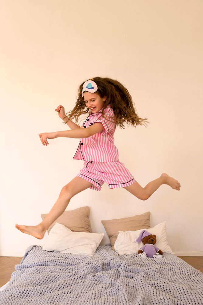 Child jumping on bed in playful mood in bedroom.