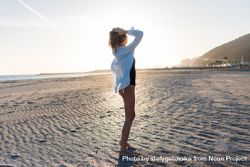 Woman with her arms up on beach in oversized shirt 49PpW5
