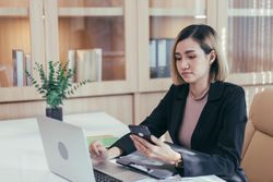 Woman checking her phone while sitting at her desk with laptop
