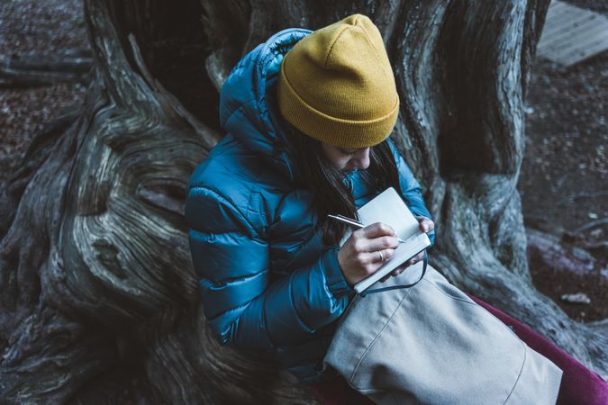 Woman sitting on tree root and writing in notebook