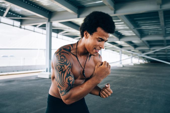 Smiling Black male athlete with tattoos doing boxing training outside