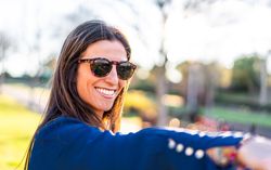 portrait of young woman with sunglasses sitting on grass in park