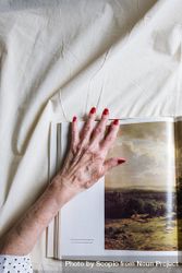 Woman's left hand on a page with natural landscape photo in a book bGQXa5