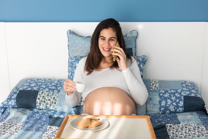 Cheerful pregnant woman speaking on smartphone during breakfast