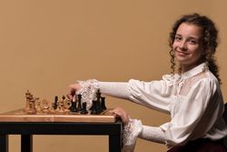 Young girl smiling while adjusting black chess pieces