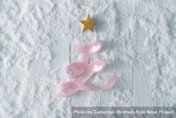 Wooden table background with snow and festive pink ribbon tree decoration 0VzNO0