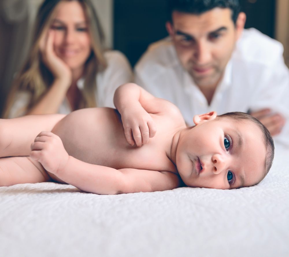Newborn lying over bed and couple smiling on background
