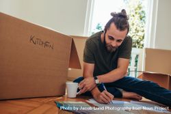 Man sitting with packing boxes around him and making a checklist 56VPL5