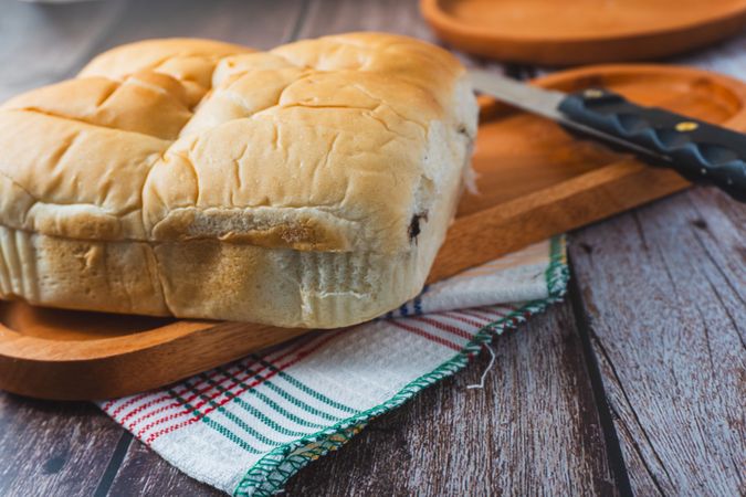 A loaf of bread served on a wooden plate placed on a rustic wooden surface