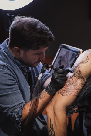 Master doing tattoo on forearm of male customer