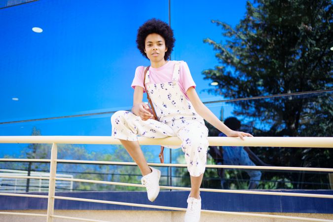 Woman sitting on handrails in front of reflective building