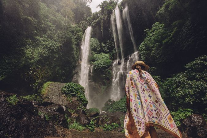 Rear view shot of female tourist walking towards waterfall in tropical rain forest
