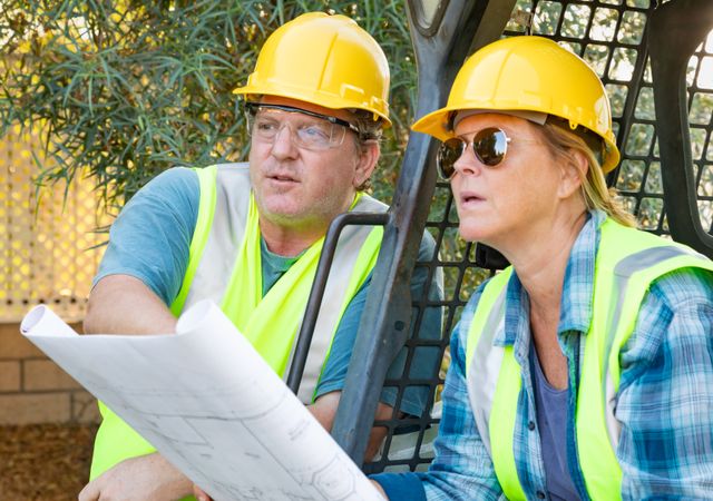Male and Female Workers With Technical Blueprints Talking at Construction Site