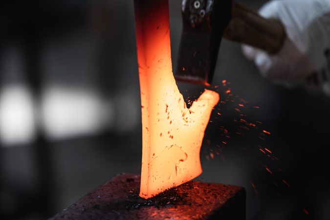 Blacksmith in gloves hot hitting metal part on anvil