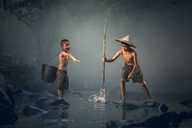 Two Asian boys fishing in shallow water in the river