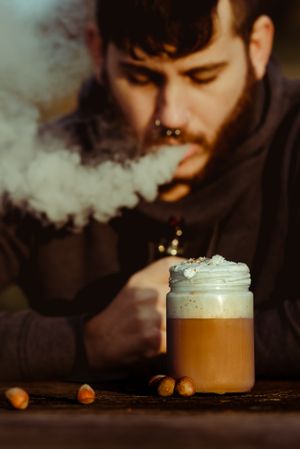 Vaper puffing smoke near a cup of fresh coffee