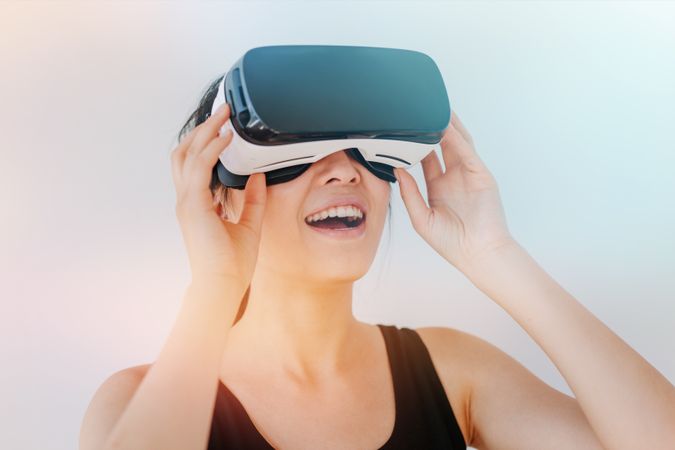 Close up shot of smiling young woman using the VR goggles against grey background