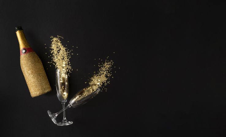 Champagne bottle with two flutes full of glitter on dark background