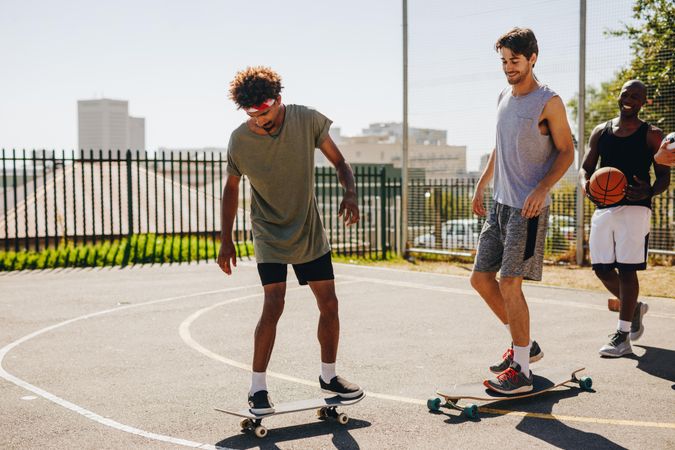 Cheerful basketball men learning to skateboard