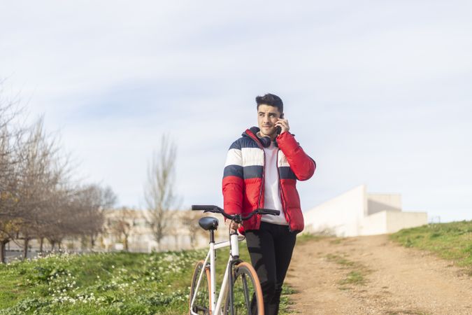 Man walking with bicycle and speaking on a smartphone in park