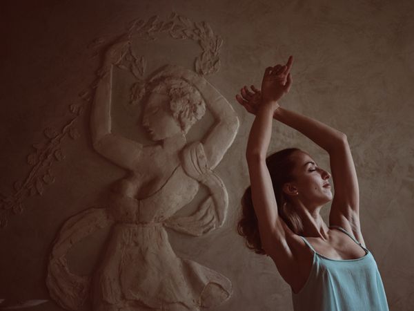 Woman with raised arms copying pose of female on relief