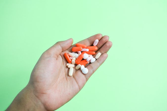 Variety of colorful medication and vitamins in person's hand above green table