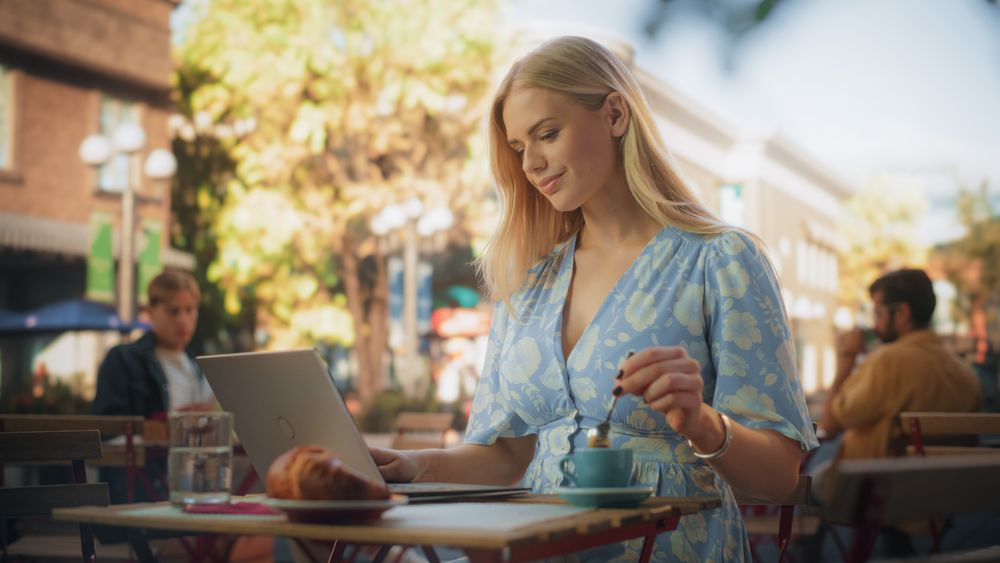 Beautiful Female Using Laptop Computer on a Terrace in a Cozy Cafe on a Summer Day.