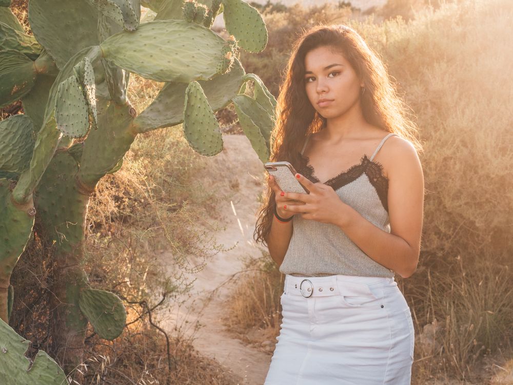 Playful trendy young woman texting at deserted countryside